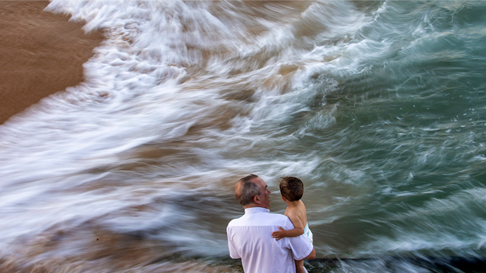 A man holds a baby as they look at the Mediterranean sea in Barcelona, Spain, July 16, 2019. 