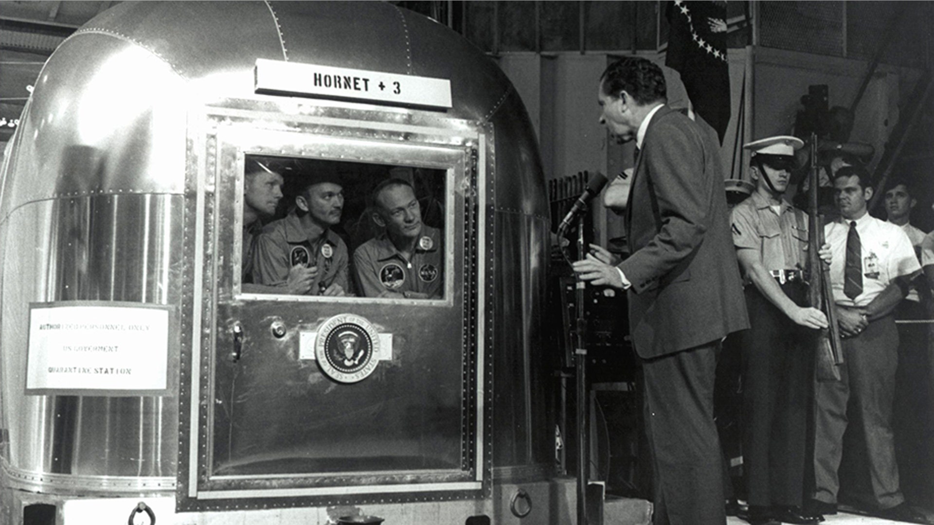 Astronauts Commander Neil Armstrong, Command Module Pilot Michael Collins and Lunar Module Pilot Buzz Aldrin talk with President Richard Nixon while in the Mobile Quarantine Facility after splashdown in the Pacific Ocean, July 24, 1969.