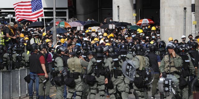 Protesters hoist a U.S. flag as they face off with riot police at the entrance to a village at Yuen Long district in Hong Kong Saturday, July 27, 2019. Thousands of protesters began marching Saturday despite police warnings that their presence would spark confrontations with local residents. Demonstrators wearing black streamed through Yuen Long, the area where a mob brutally attacked people in a commuter rail station last Sunday.