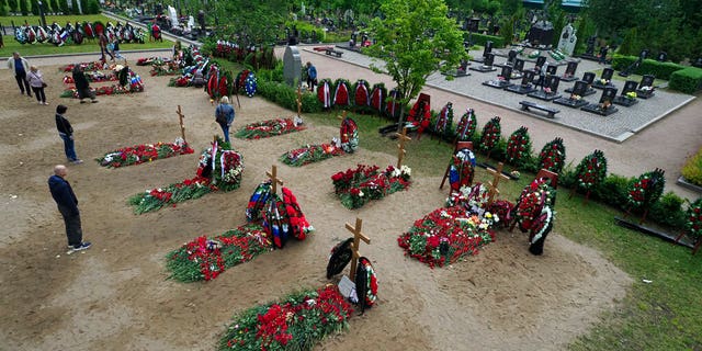 People lay flowers at the graves of the 14 crew members who died in a fire on a Russian navy's deep-sea research submersible, next to the graves of crew members of Kursk submarine, right, at the Serafimovskoye memorial cemetery during a funeral ceremony in St. Petersburg, Russia, Saturday, July 6, 2019.
