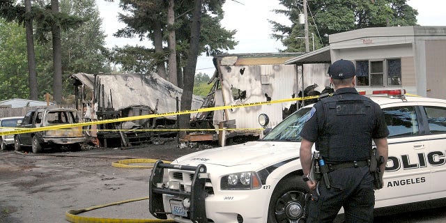 Port Angeles police Officer T.J. Mueller looks over the scene of a fire that destroyed two mobile homes and left several dead early Saturday, July 6, 2019. (Associated Press)