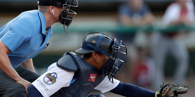 Umpire Brian deBrauwere huddles behind Freedom Division catcher James Skelton, of the York Revolution, as the official wears an earpiece during a minor league game on July 10, 2019, in York, Pennsylvania.