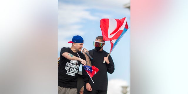 El rapero puertorriqueño René Juan Pérez conocido por su nombre artístico de Residente, a la izquierda, habla a la multitud frente al Capitolio de Puerto Rico en San Juan el miércoles (Foto AP / Dennis M. Rivera Pichardo)