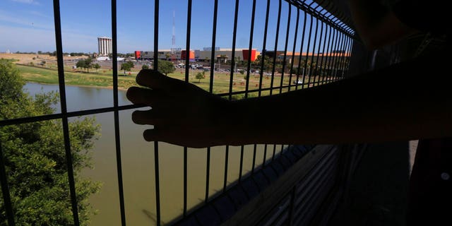 The hand of a youth from Nuevo Laredo rests on the gate as he stops to watch a train pass, above the Rio Grande river on International Bridge 1 Las Americas, a legal port of entry which connects Laredo, Texas in the U.S. with Nuevo Laredo, Mexico, Thursday, July 18, 2019.