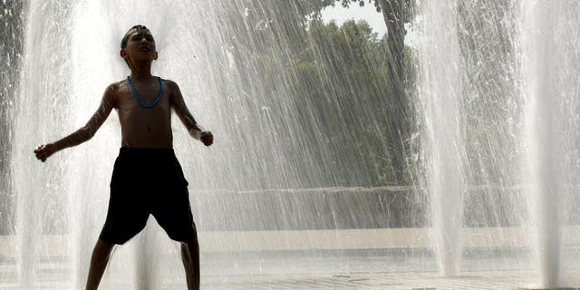 A boy plays in a fountain to cool off as temperatures approach 100 degrees Thursday, July 18, 2019, in Kansas City, Mo. 