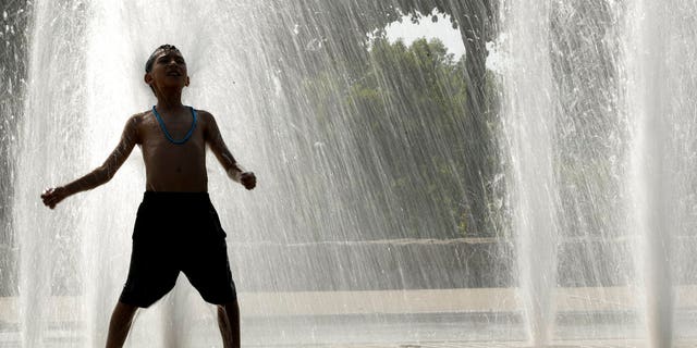 A boy plays in a fountain to cool off as temperatures approach 100 degrees Thursday, July 18, 2019, in Kansas City, Mo.