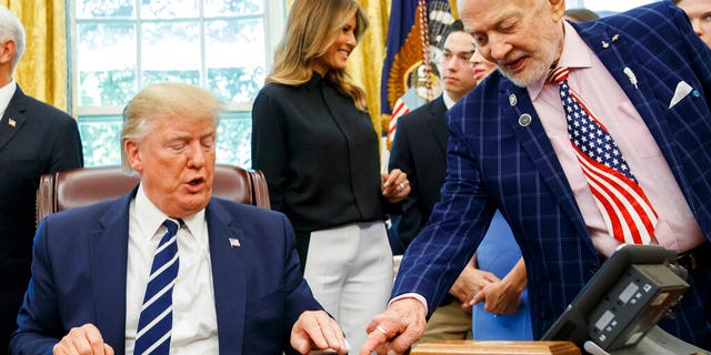 President Donald Trump receives a gift from Apollo 11 astronaut Buzz Aldrin, with first lady Melania Trump, during a photo opportunity commemorating the 50th anniversary of the Apollo 11 moon landing in the Oval Office of the White House, Friday, July 19, 2019, in Washington.