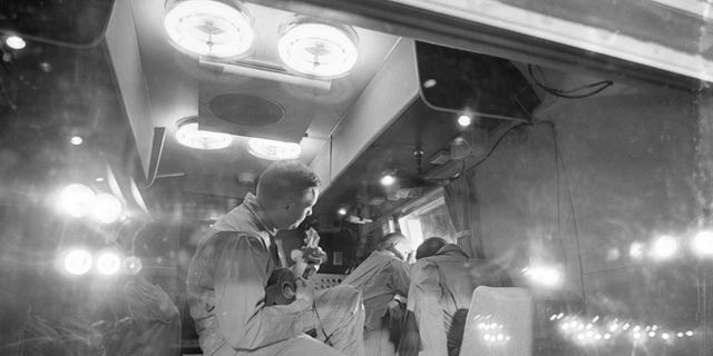 An interior view of the Mobile Quarantine Facility shows the Apollo 11 crew after their arrival at Ellington Air Force Base. Mission Commander Neil Armstrong is strumming on a ukulele while Michael Collins (right foreground) and Buzz Aldrin (right background) are looking out the window. The other people in the picture are MQF support personnel.