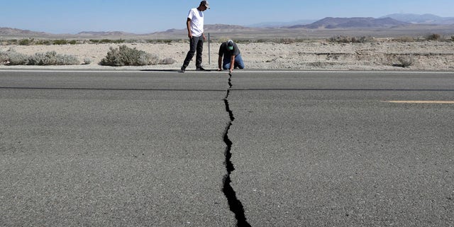 Ron Mikulaco, right, and his nephew, Brad Fernandez, examine a crack caused by an earthquake on Highway 178, Saturday, July 6, 2019, outside of Ridgecrest, Calif.