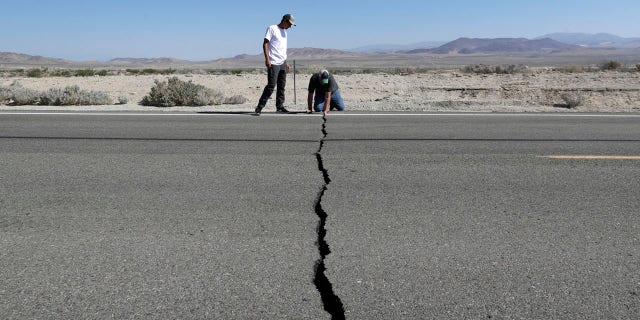 Ron Mikulaco, right, and his nephew, Brad Fernandez, examine a crack caused by an earthquake on Highway 178, Saturday, July 6, 2019, outside of Ridgecrest, Calif.