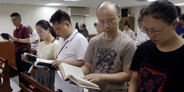 In this Sunday, July 7, 2019, photo, from right; Ren Dejun, Liao Qiang, Peng Ran and Ren Ruiting follow a hymn book during service at a church in Taipei, Taiwan. The Sunday service this week at an unassuming church in Taiwan was especially moving for one man, Liao Qiang. It was the first time he had worshipped publicly since authorities shut down his church in China seven months ago. (AP Photo/Chiang Ying-ying)