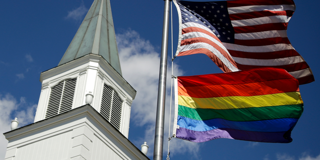 In this April 19, 2019 file photo, a gay pride rainbow flag flies along with the U.S. flag in front of the Asbury United Methodist Church in Prairie Village, Kan. A new Associated Press-NORC Center for Public Affairs Research poll shows age, education level and religious affiliation matter greatly when it comes to Americans’ opinions on a prospective clergy member’s sexual orientation, gender, marital status or views on issues such as same-sex marriage or abortion 