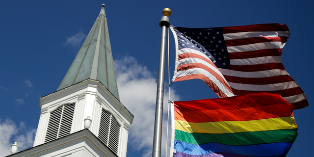 In this April 19, 2019 file photo, a gay pride rainbow flag flies along with the U.S. flag in front of the Asbury United Methodist Church in Prairie Village, Kan. A new Associated Press-NORC Center for Public Affairs Research poll shows age, education level and religious affiliation matter greatly when it comes to Americans’ opinions on a prospective clergy member’s sexual orientation, gender, marital status or views on issues such as same-sex marriage or abortion