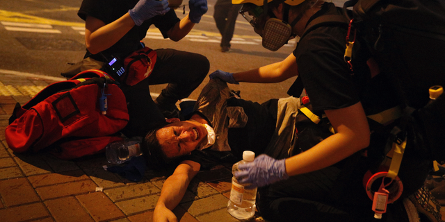 FILE - In this file photo taken Sunday, July 21, 2019, medical workers help a protester in pain from tear gas fired by policemen on a street in Hong Kong. The former British colony of Hong Kong was returned to China in 1997 under a “one country, two systems” concept that gives the city a fair degree of autonomy over its affairs, but China may intervene to quell protests now in their seventh week. (AP Photo/Bobby Yip, File)