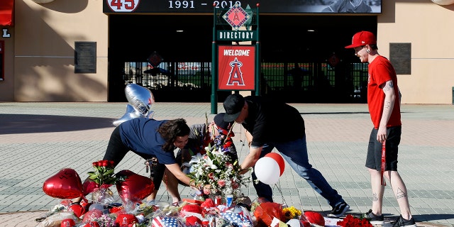 Los Angeles Angels fans prop up a memorial to give their condolences for pitcher Tyler Skaggs at Angel Stadium in Anaheim, Calif., Monday, July 1, 2019. Skaggs died at the age of 27, stunning Major League Baseball and leading to the postponement of the team's game against the Texas Rangers on Monday. (AP Photo/Alex Gallardo)