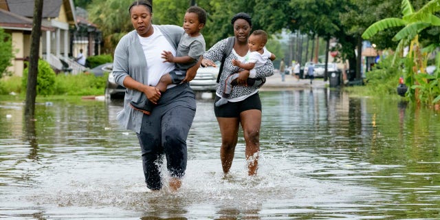 Jalana Furlough carries her son Drew Furlough as Terrian Jones carries Chance Furlough on Belfast Street near Eagle Street in New Orleans after flooding from a tropical wave system in the Gulf Mexico that dumped lots of rain in Wednesday, July 10, 2019.