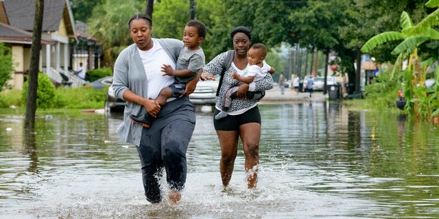 Jalana Furlough carries her son Drew Furlough as Terrian Jones carries Chance Furlough on Belfast Street near Eagle Street in New Orleans after flooding from a tropical wave system in the Gulf Mexico that dumped lots of rain in Wednesday, July 10, 2019.