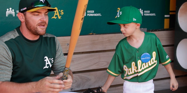 Eight-year-old August Wold waits for Oakland Athletics' Liam Hendriks to finish taping his bat in the dugout. (AP Photo/Ben Margot)