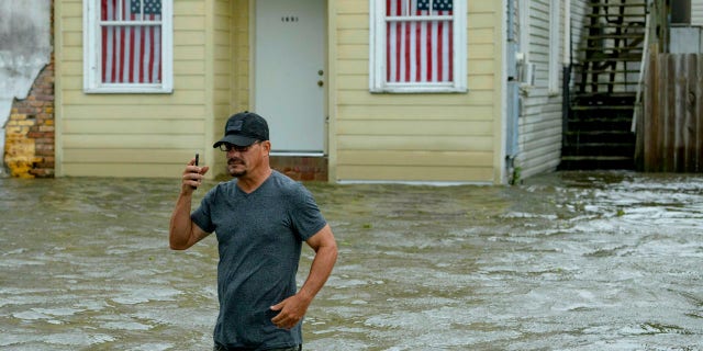 Barry Williams talks to a friend on his smartphone as he wades through storm surge from Lake Pontchartrain on Lakeshore Drive in Mandeville, La.