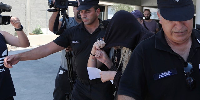 Elite police unit officers escort a 19-year old British woman, center with head covered, to Famagusta court in Paralimni, Cyprus. (AP Photo/Petros Karadjias)