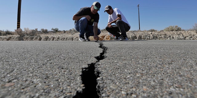 Ron Mikulaco, left, and his nephew, Brad Fernandez, examine a crack caused by an earthquake on highway 178 outside Ridgecrest, Calif. (AP Photo/Marcio Jose Sanchez)