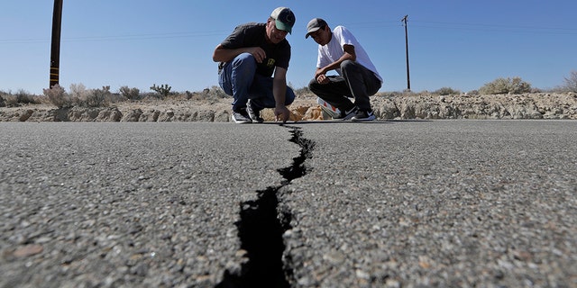 Ron Mikulaco, left, and his nephew, Brad Fernandez, examine a crack caused by an earthquake on highway 178 Saturday, July 6, 2019, outside of Ridgecrest, Calif. Crews in Southern California assessed damage to cracked and burned buildings, broken roads, leaking water and gas lines and other infrastructure Saturday after the largest earthquake the region has seen in nearly 20 years jolted an area from Sacramento to Las Vegas to Mexico. (AP Photo/Marcio Jose Sanchez)