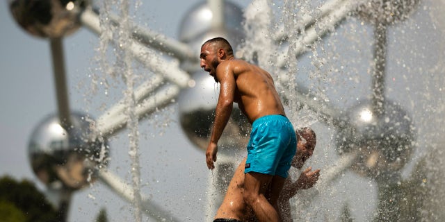 Two men cool off in a public fountain near the Atomium during a summer hot day in Brussels, Wednesday, July 24, 2019.