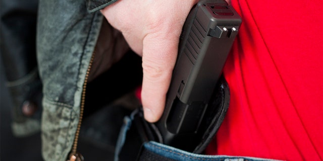 A man drawing his modern polymer (Glock) .45 caliber pistol from an IWB (inside the waistband) holster under his leather jacket.