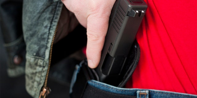 A man drawing his modern polymer Glock .45 caliber pistol from an inside the waistband holster under his leather jacket.