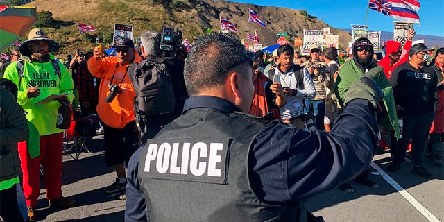 A police officer gestures at demonstrators blocking a road at the base of Hawaii's tallest mountain, on Monday, in Mauna Kea, Hawaii, who are protesting the construction of a giant telescope on land that some Native Hawaiians consider sacred. (AP)