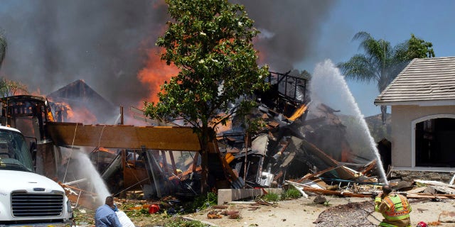 A firefighter and civilians train fire hoses on a burning home after an explosion and fire destroyed the home in Murrieta, Calif., sending up thick flames and closing several streets. One Southern California Gas Company employee was killed.
