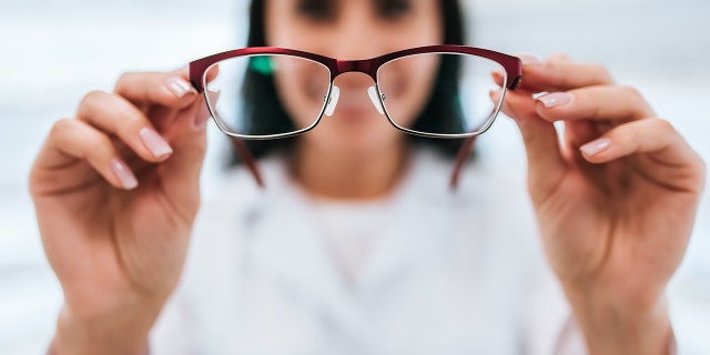 Cropped image of attractive young female doctor in ophthalmology clinic. Doctor ophthalmologist is standing near shelves with different eyeglasses.