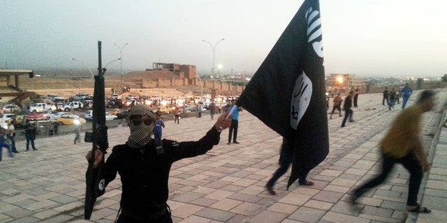 A fighter of the Islamic State of Iraq and the Levant (ISIL) holds an ISIL flag and a weapon on a street in the city of Mosul, June 23, 2014. U.S. Secretary of State John Kerry held crisis talks with leaders of Iraq's autonomous Kurdish region on Tuesday urging them to stand with Baghdad in the face of a Sunni insurgent onslaught that threatens to dismember the country.