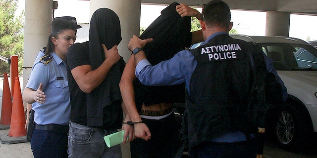 Israeli men cover their faces with their shirts as they arrive at the Famagusta courthouse in Paralimni town, Cyprus, Thursday, July 18, 2019. A Cyprus court has ordered 12 Israelis vacationing on the east Mediterranean island nation to remain in police custody for eight days after a 19-year-old British woman alleged that she was raped.