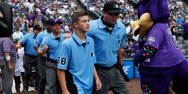 Thirteen-year-old Josh Cordova, left, of Denver, heads on the diamond with home plate umpire Cory Blaser before the Colorado Rockies host the Los Angeles Dodgers in the first inning of a baseball game Sunday, June 30, 2019, in Denver. The young man was officiating a youth baseball game when a brawl broke out among adults in the nearby suburb of Lakewood, Colo. (AP Photo/David Zalubowski)