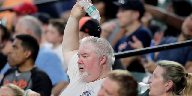 The spectator drops water on his head while watching the fourth move of a baseball match between Baltimore Orioles and Boston Red Sox in hot weather on Saturday, July 20, 2019, in Baltimore.