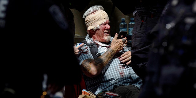 A man checks his phone while surrounded by police and medics after being injured during a civil disturbance in Portland, Ore., on Saturday, June 29, 2019. (Associated Press)