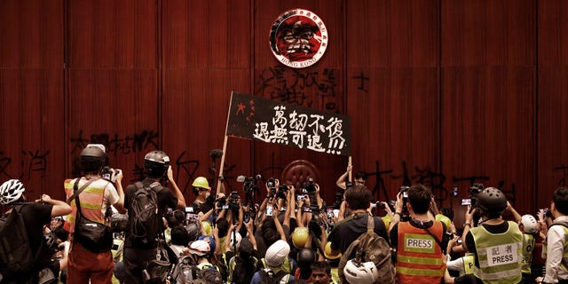 Protesters raise a banner reads "Beyond redemption, no retreat" in front of a defaced Hong Kong logo after break in at the Legislative Chamber to protest against the extradition bill in Hong Kong, Monday, July 1, 2019.
