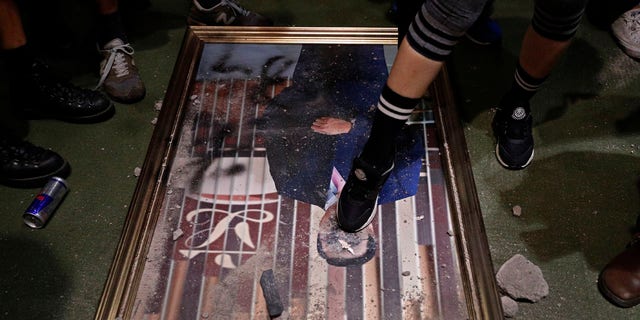 A protester steps on a damaged portrait of former legislative leader lie on the ground after protesters broke into the Legislative Council building in Hong Kong, Monday, July 1, 2019.
