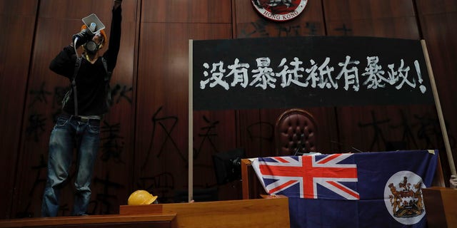 A protester shouts next to a defaced Hong Kong emblem and a banner reads "No thug, only tyranny" after they broke into the Legislative Council building in Hong Kong, Monday, July 1, 2019.