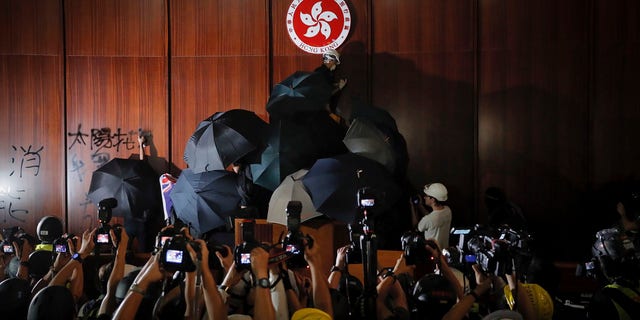 Journalists film a protester defaces the Hong Kong emblem inside the meeting hall of the Legislative Council in Hong Kong, Monday, July 1, 2019.