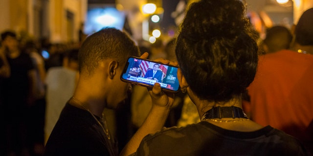 Locals listen on a smartphone to the pre-recorded message by Puerto Rico Gov. Ricardo Rossello announcing that he is resigning Aug. 2 after weeks of protests over leaked obscene, misogynistic online chats, in San Juan, Puerto Rico, Wednesday, July 24, 2019. (Associated Press)