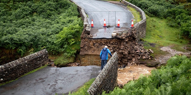 A man looks from the edge of a collapsed road bridge near Grinton, North Yorkshire, after parts of the region were inundated by overnight rain. (Danny Lawson/PA via AP)