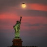 The moon rises above the Statue of Liberty in New York City, July 15, 2019.