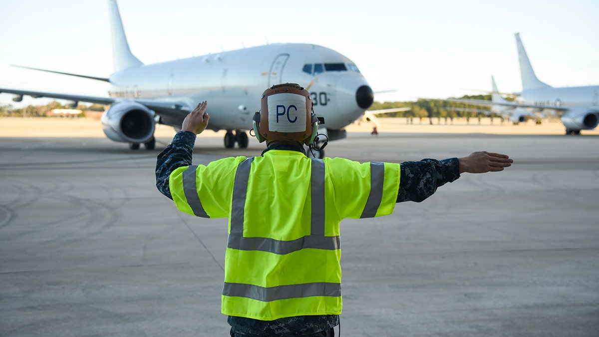 Aviation Machinist Mate 3rd Class Benjamin Harrell signals the crew of a P-8A Poseidon patrol aircraft. (U.S. Navy photo by Mass Communication Specialist 2nd Class Sean R. Morton/Released)