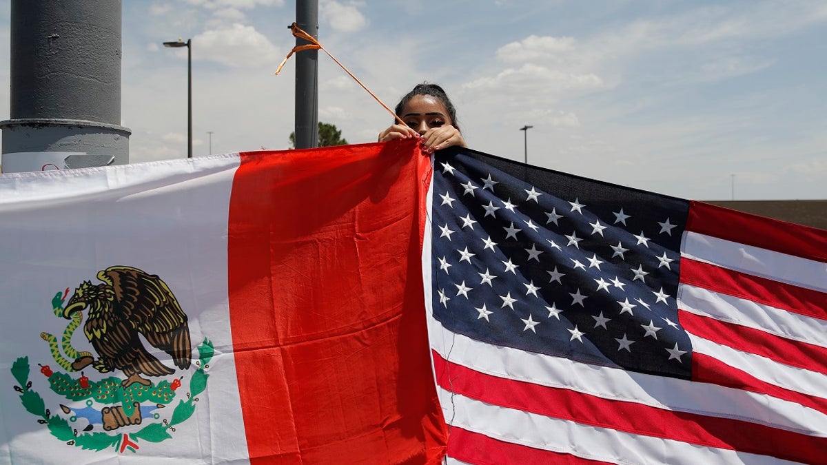 Maylin Reyes hangs a Mexican flag at a makeshift memorial near the scene of a mass shooting at a shopping complex Monday, Aug. 5, 2019, in El Paso, Texas. (AP Photo/John Locher)