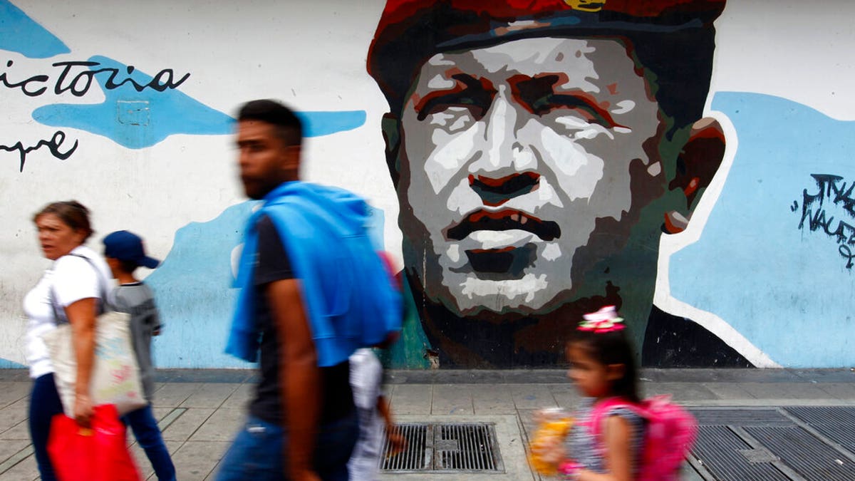 Pedestrians walk past a mural depicting the late President Hugo Chavez, in Caracas, Venezuela, Tuesday, Aug. 6, 2019. (AP Photo/Leonardo Fernandez)