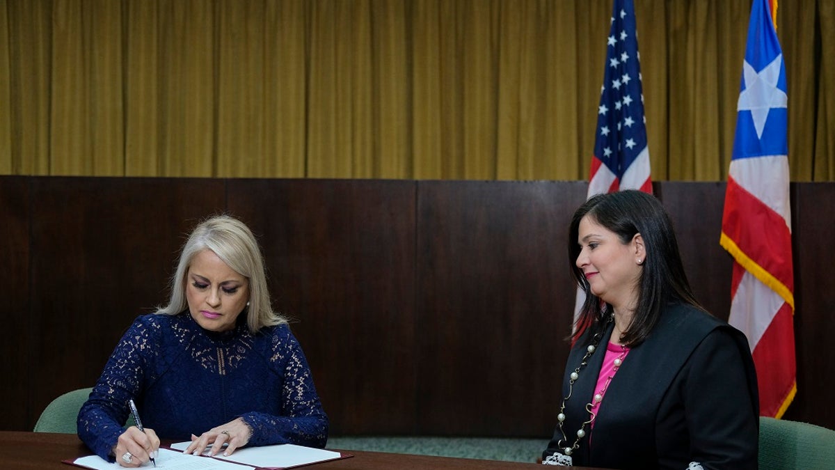 Justice Secretary Wanda Vazquez signs a document after she was sworn in as governor of Puerto Rico by Supreme Court Justice Maite Oronoz, right, in San Juan, Puerto Rico on Wednesday. (AP Photo/Dennis M. Rivera Pichardo)