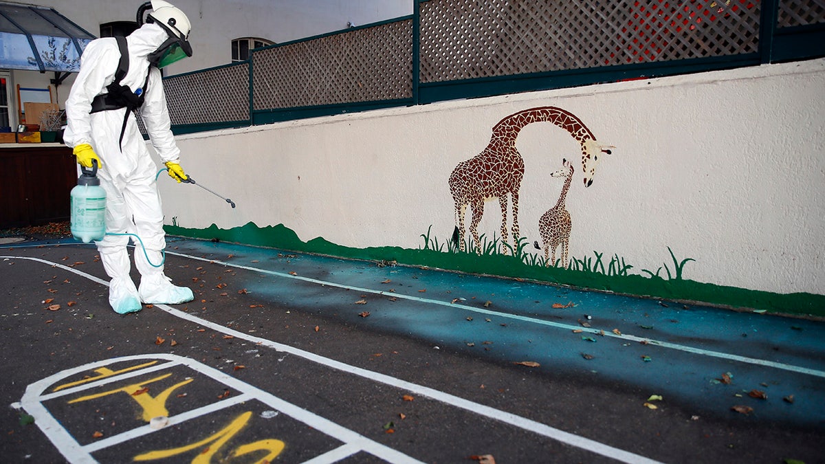 A worker sprays an adhesive product on the ground to gather up the lead particles in the schoolyard of Saint Benoit primary school in Paris, France, Thursday, Aug. 8, 2019. Workers have started decontaminating some Paris schools tested with unsafe levels of lead following the blaze at the Notre Dame Cathedral, as part of efforts to protect children from risks of lead poisoning.