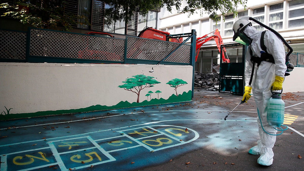 A worker sprays an adhesive product on the ground to gather up the lead particles in the schoolyard of Saint Benoit primary school in Paris, France, Thursday, Aug. 8, 2019. Workers have started decontaminating some Paris schools tested with unsafe levels of lead following the blaze at the Notre Dame Cathedral, as part of efforts to protect children from risks of lead poisoning. (AP Photo/Francois Mori)